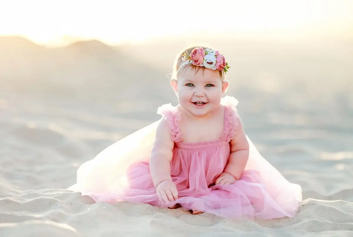 Baby girl in a pink dress sitting on the sand at golden hour