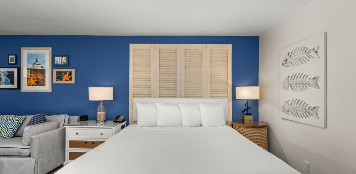 Paradise Point Resort bungalow bedroom with coastal blue accent wall, white bedding, and shutter-style headboard