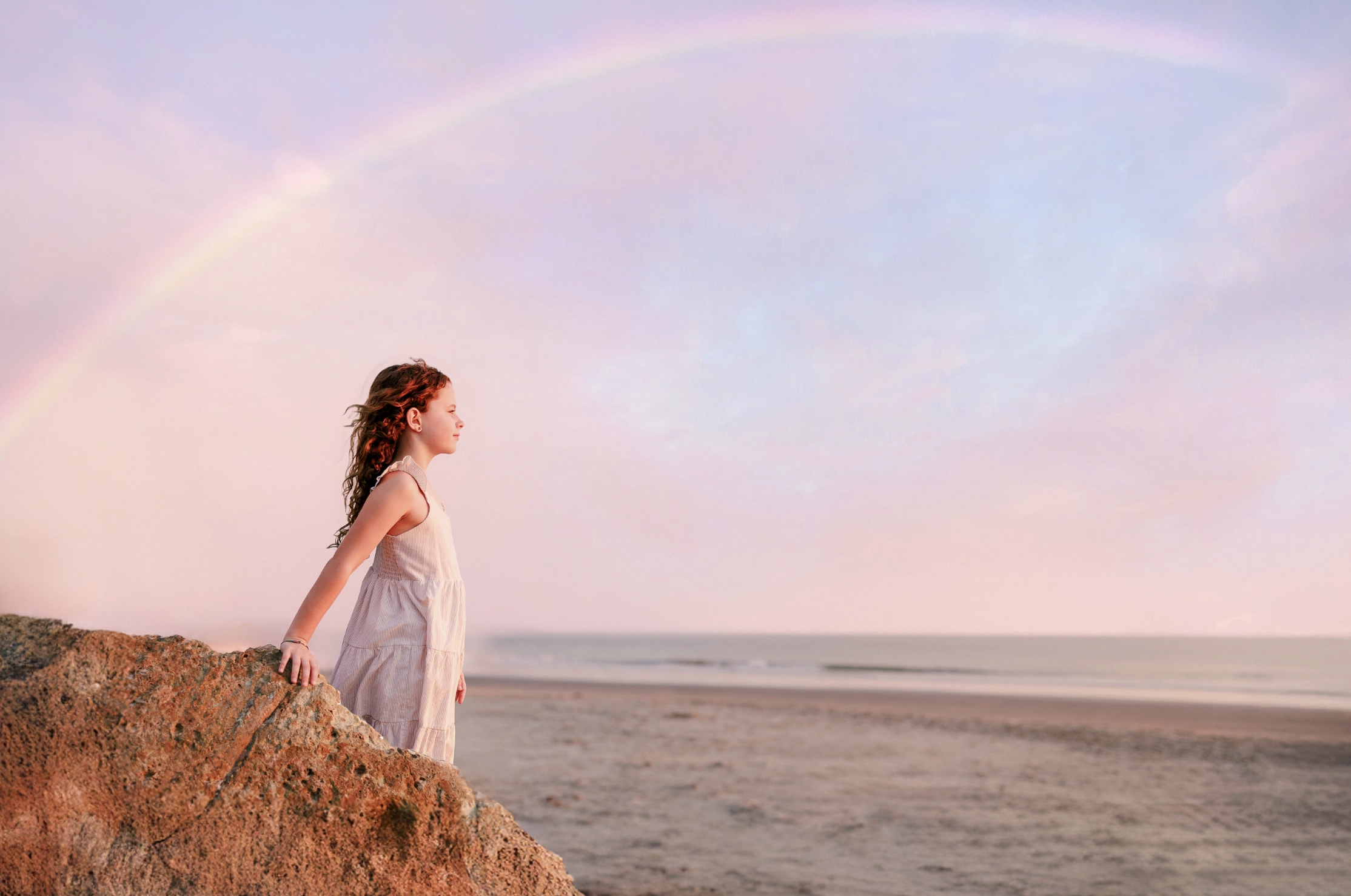 Girl watching the ocean under a rainbow in a pink evening sky on Coronado Beach