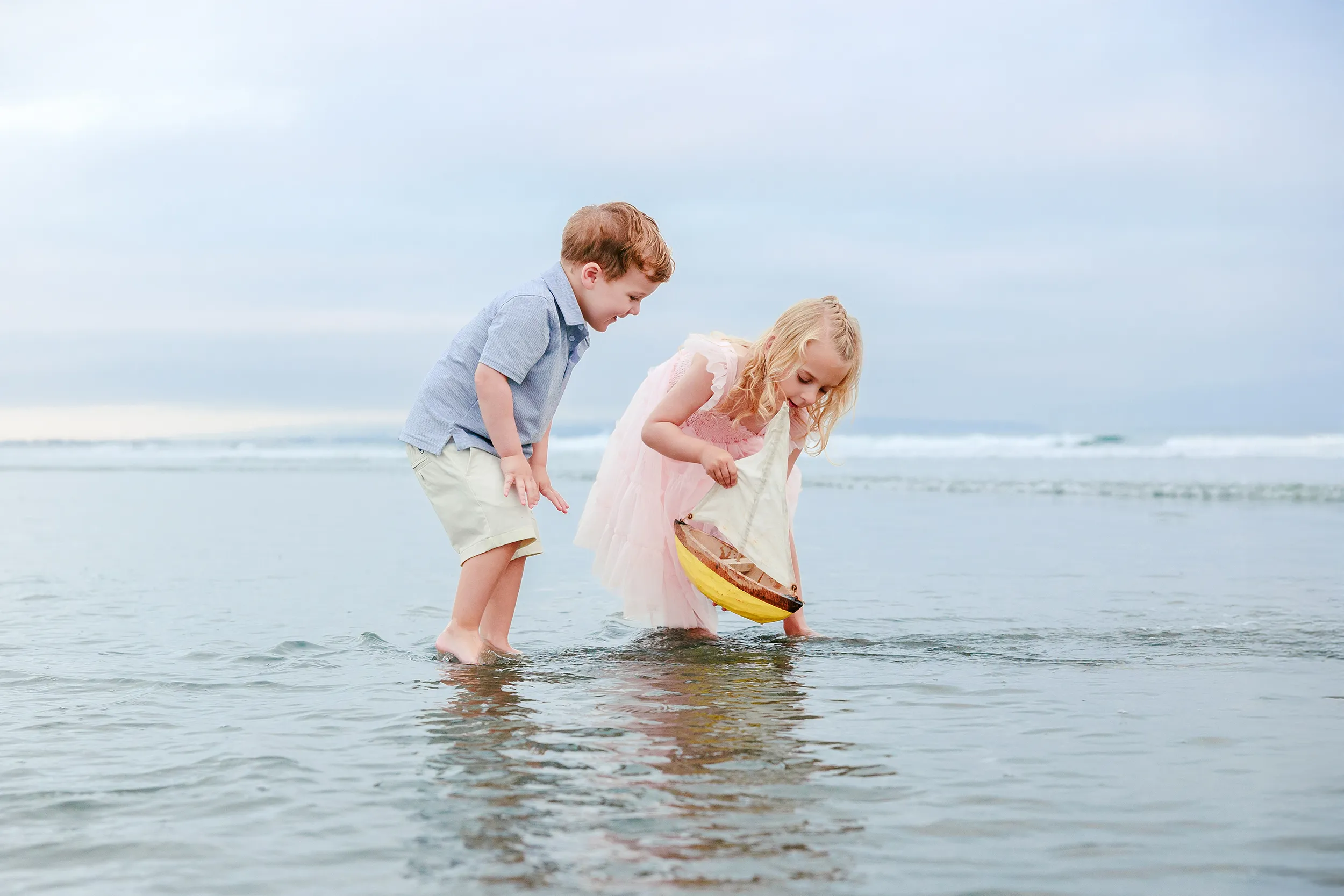 Two kids sailing a toy boat in the gentle shallows on Coronado Beach
