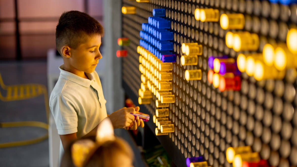 A child placing colored pegs into a glowing Lite-Brite wall at a San Diego museum