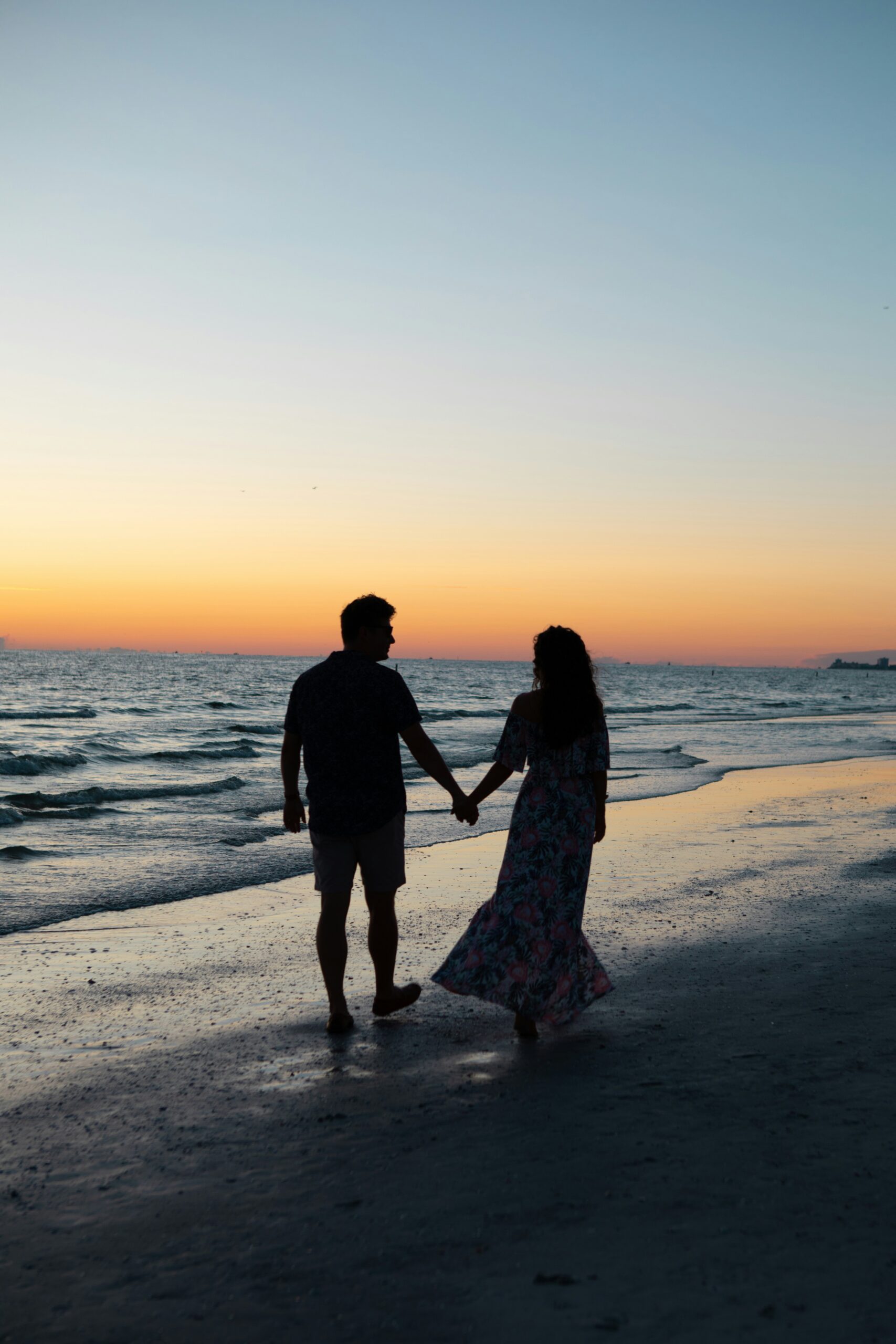 A couple walking hand in hand on the beach at sunset