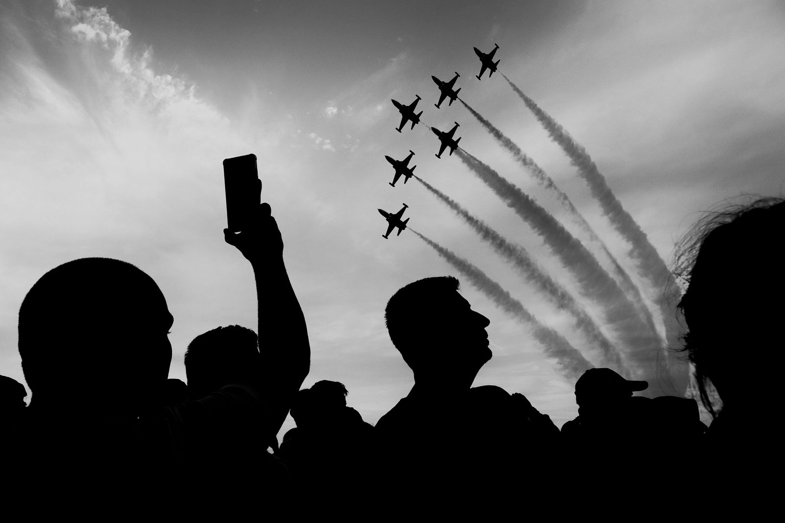 Silhouetted crowd looking up and photographing an aircraft passing overhead at an air show