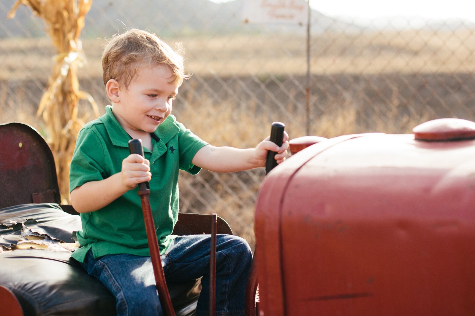 A young boy in a green shirt steering an old red tractor at Oma’s Family Farm