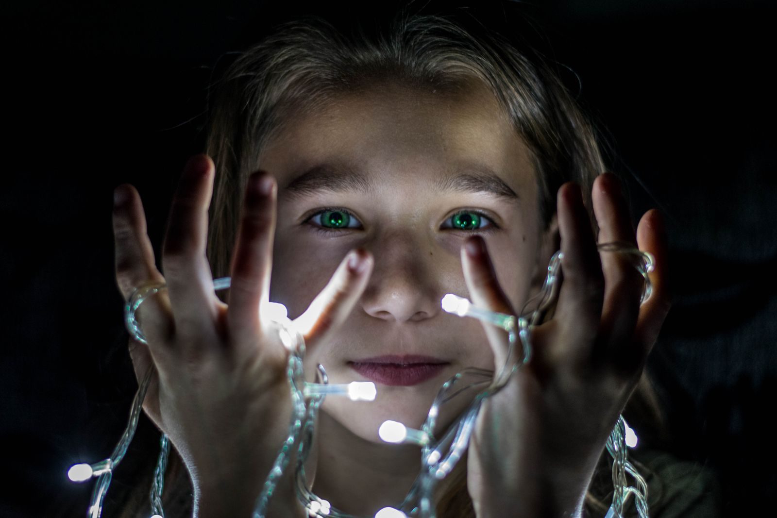 Young girl holding a strand of glowing string lights up to her face