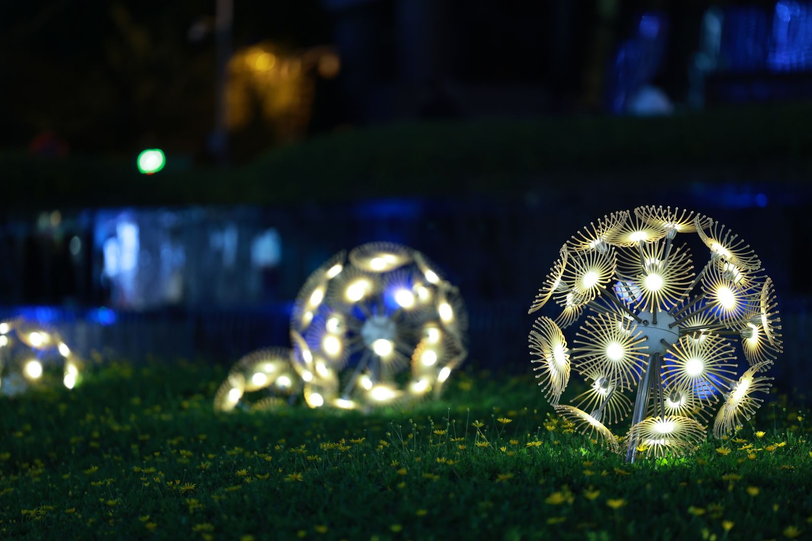 Glowing dandelion-shaped light spheres sitting on a grassy lawn at night