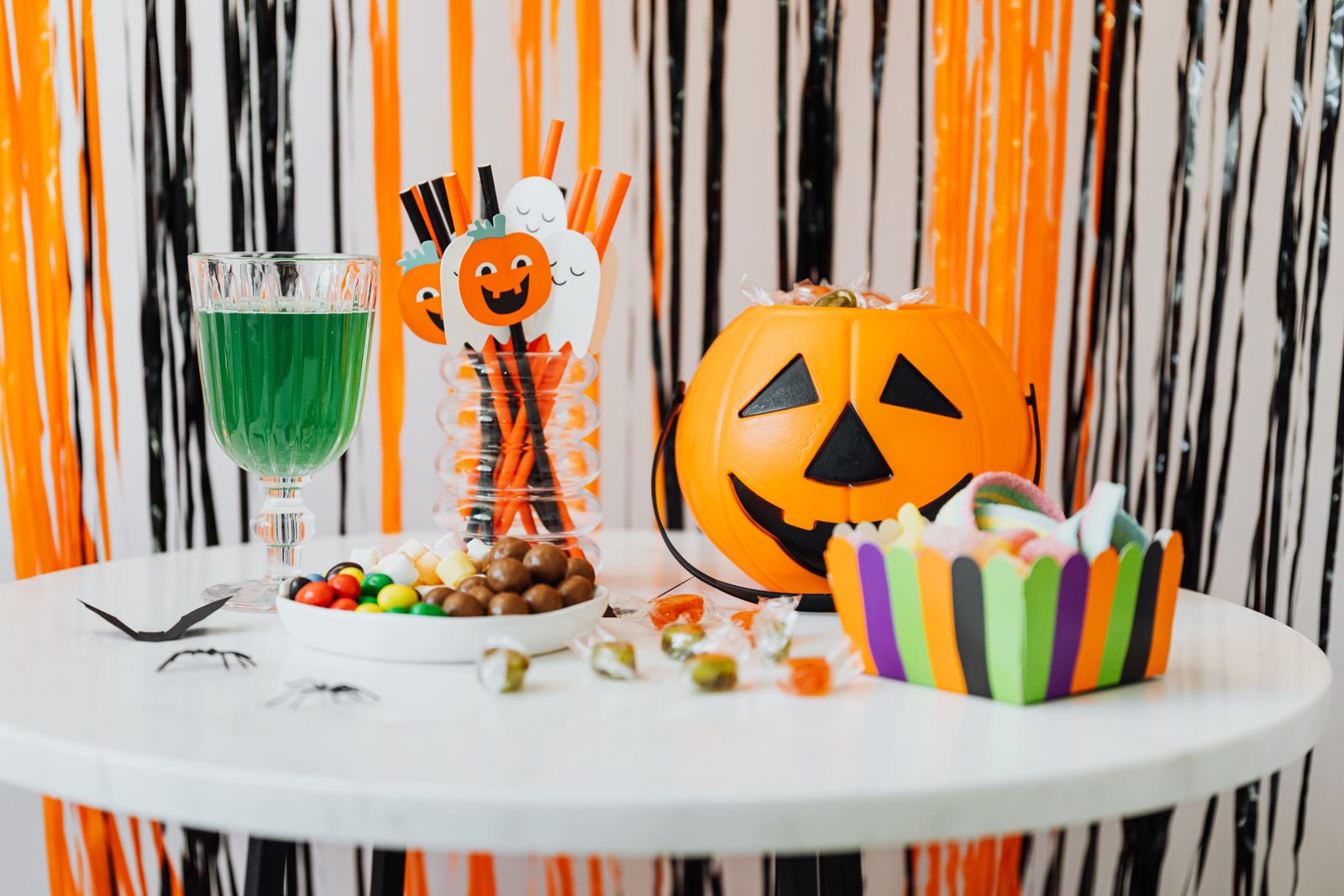 Halloween candy spread on a table beside a jack-o-lantern treat bucket