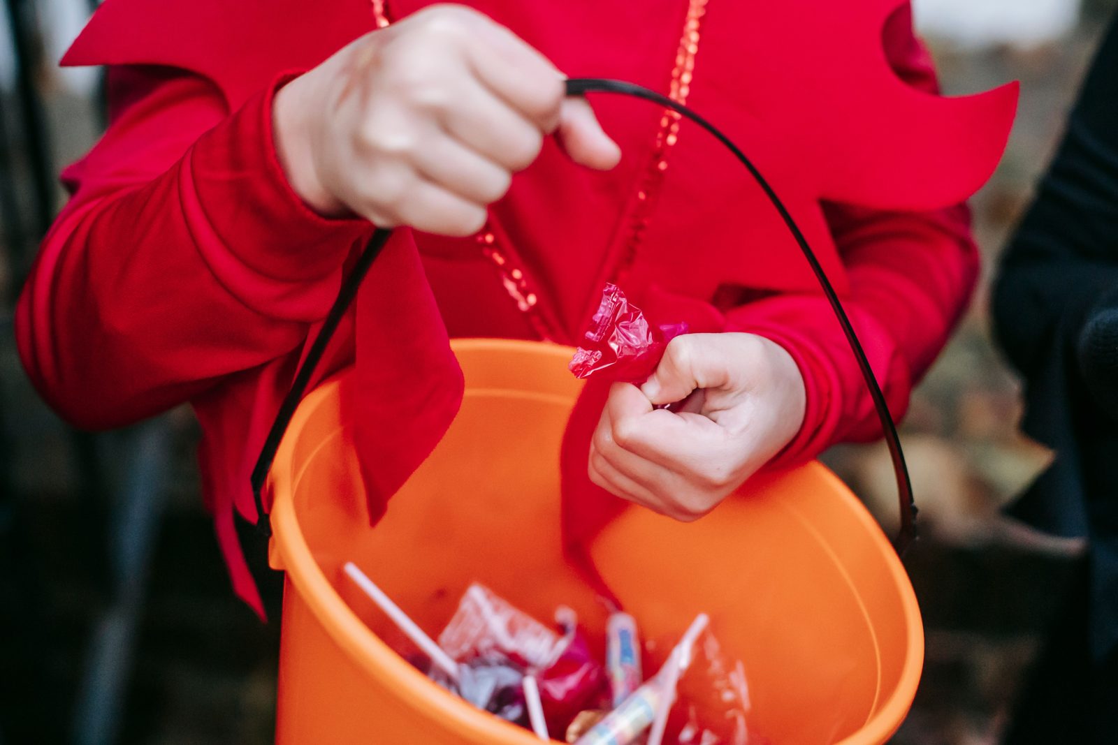 Child in a Halloween costume holding a plastic bucket filled with candy