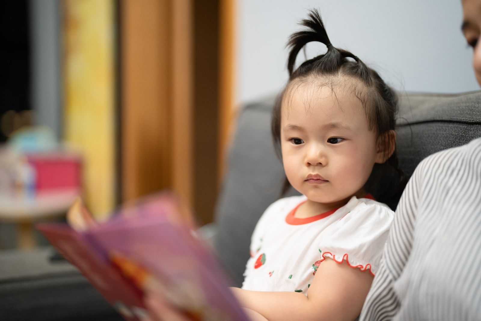 Toddler on a sofa listening while someone reads a picture book aloud