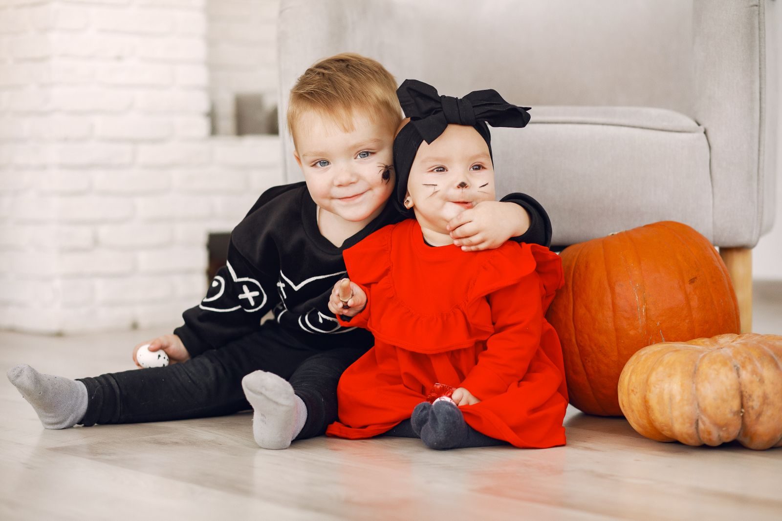 Two toddlers in Halloween costumes sitting with pumpkins